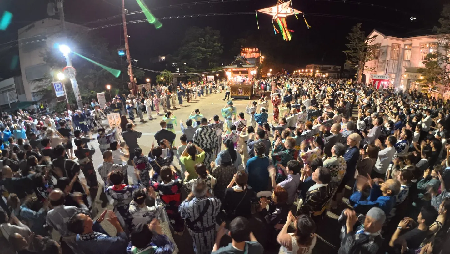 Opening night 2026: concentric rings of dancers, in yukata and everyday clothes alike, circling the lantern-lit yakata float in front of the old town hall, under a star-shaped festival lantern