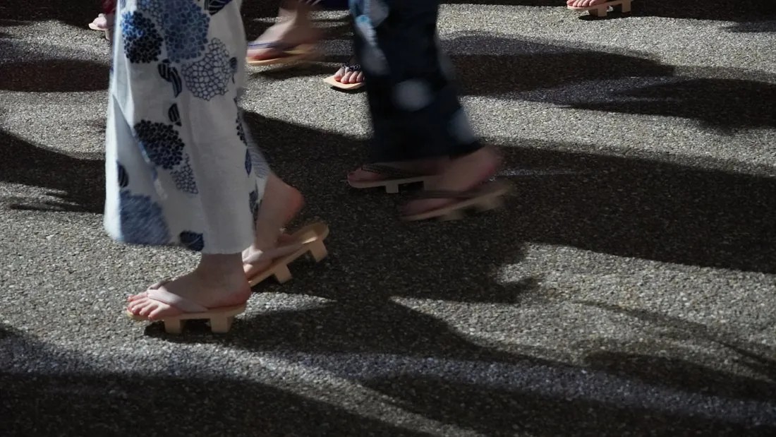 Dancers' feet mid-step on the asphalt: wooden geta with bare feet beside them, motion-blurred in the middle of the dance