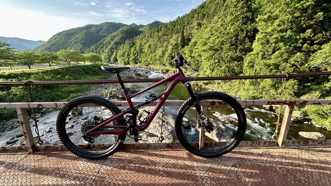 Mountain bike on a weathered bridge over a crystal-clear river, lush green valley stretching into the distance