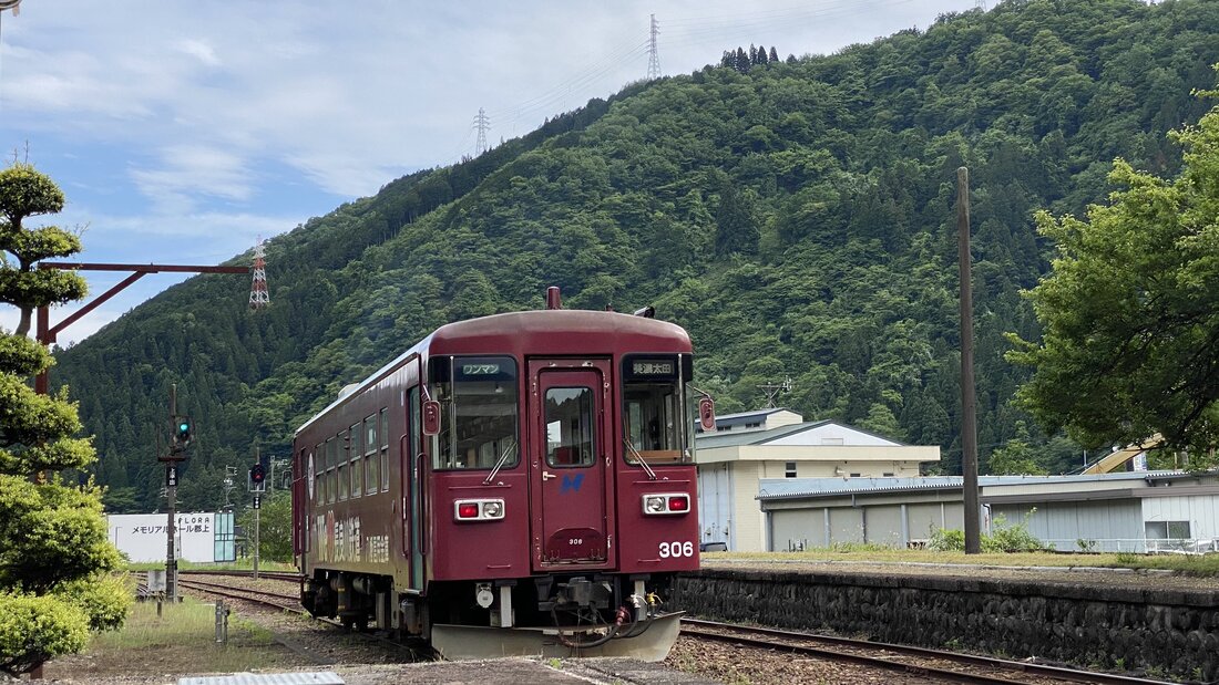 Nagaragawa Railway train No. 306 at a rural station, forested mountain rising behind it