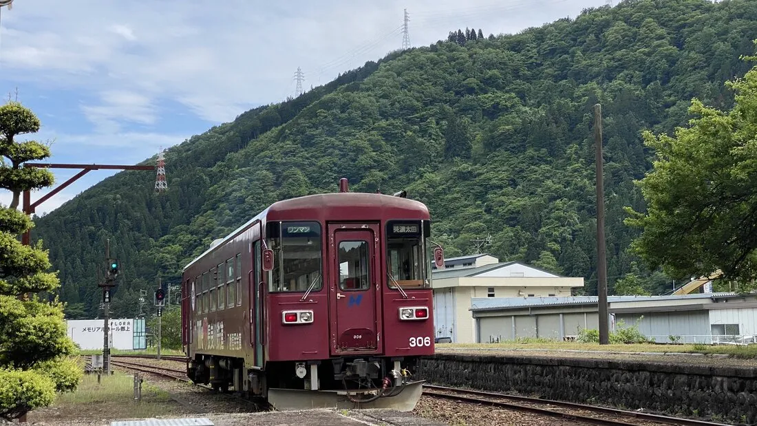 Nagaragawa Railway train No. 306 at a rural station, forested mountain rising behind it