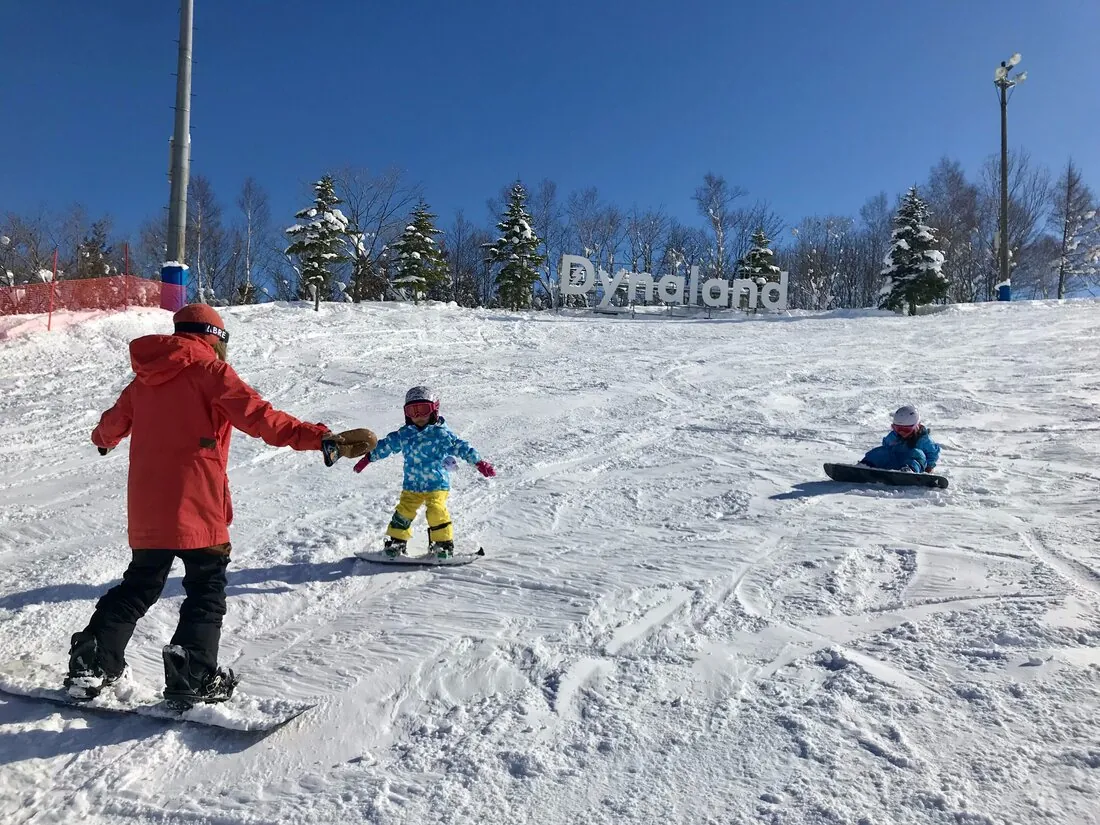 A family skiing at Dynaland on a clear winter day, with the resort's logo sign visible in the background